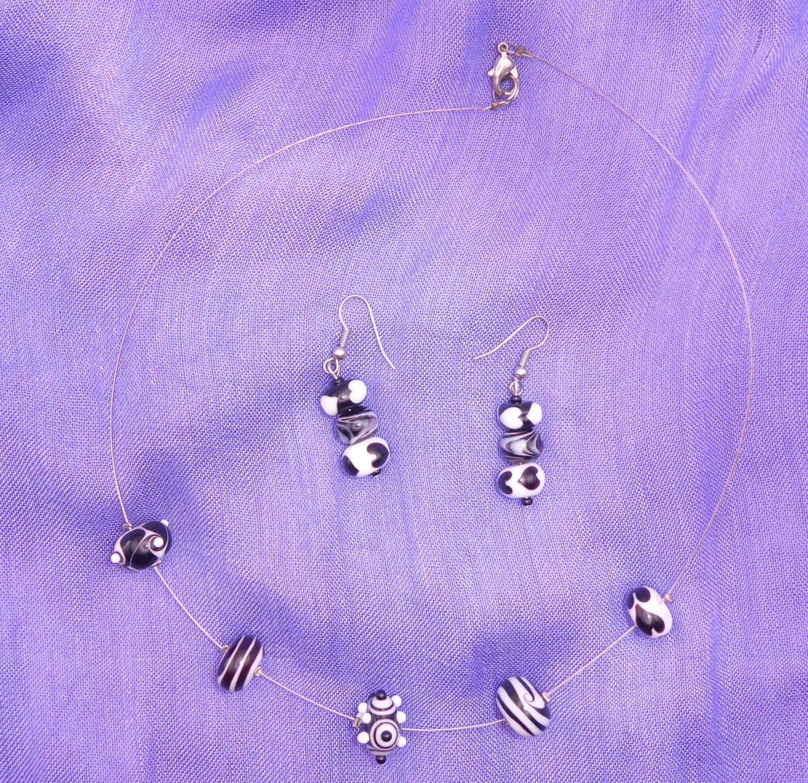 Glasperlenkette und Ohrringe mit schwarz-weißen Perlen auf violettem Stoff