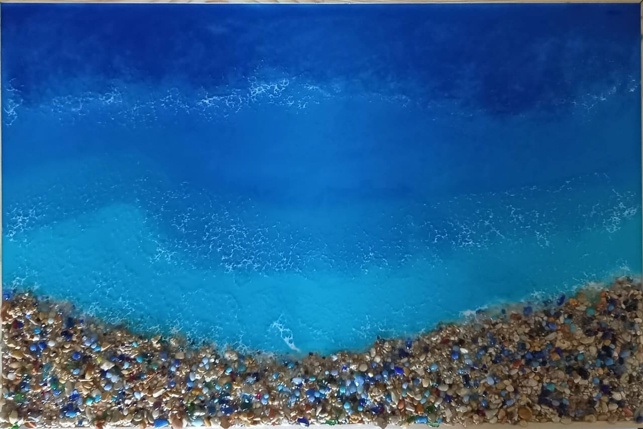 Resin-Bild: tiefblaues Meer wird zum Ufer hin türkis, der Strand besteht aus bunten Glas- und Kieselsteinen