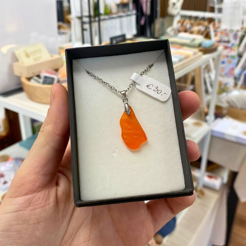 Oranger Meerglas-Anhänger an einer Edelstahlkette in einer Schmuckschachtel